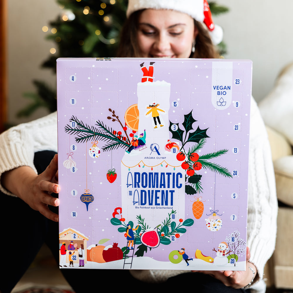 Aroma Olymp – Frau mit Weihnachtsmütze hält den Bio Feinkost Adventskalender Vegan 2025 Aromatic Advent.