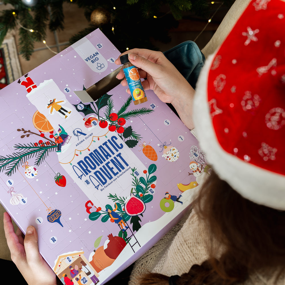 
                  
                    Aroma Olymp – Frau mit Weihnachtsmütze öffnet den Bio Feinkost Adventskalender Vegan 2025 und entnimmt eine Balsamico-Creme.
                  
                