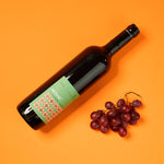 Aroma Olymp Bio Rotwein "Mosaic". Präsentiert auf orangenem Grund, daneben rote Trauben.